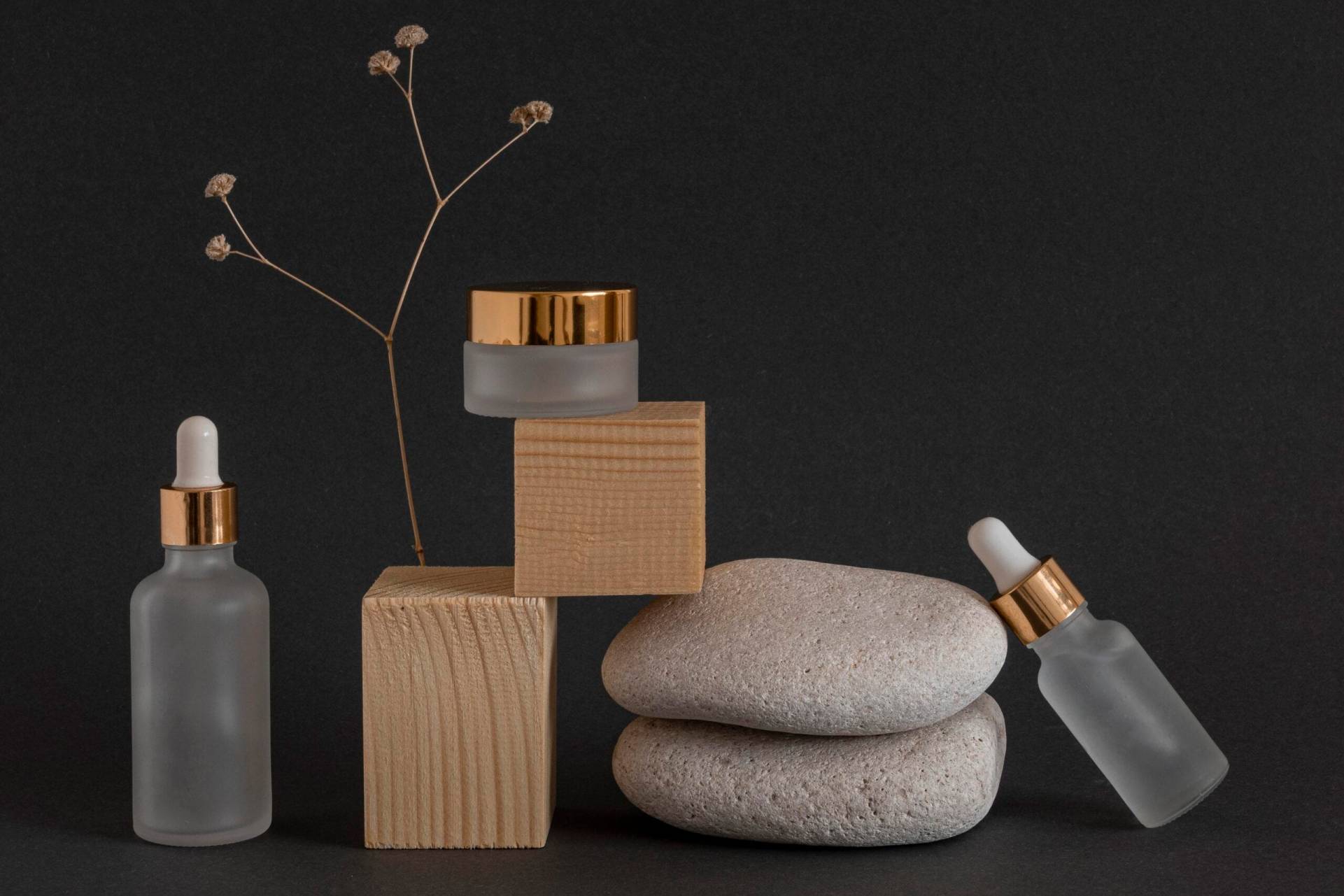 Luxury Skincare on Stone Display – Valentine Aura Luxe Luxury frosted glass skincare serum bottles with gold accents on stacked stones against dark background