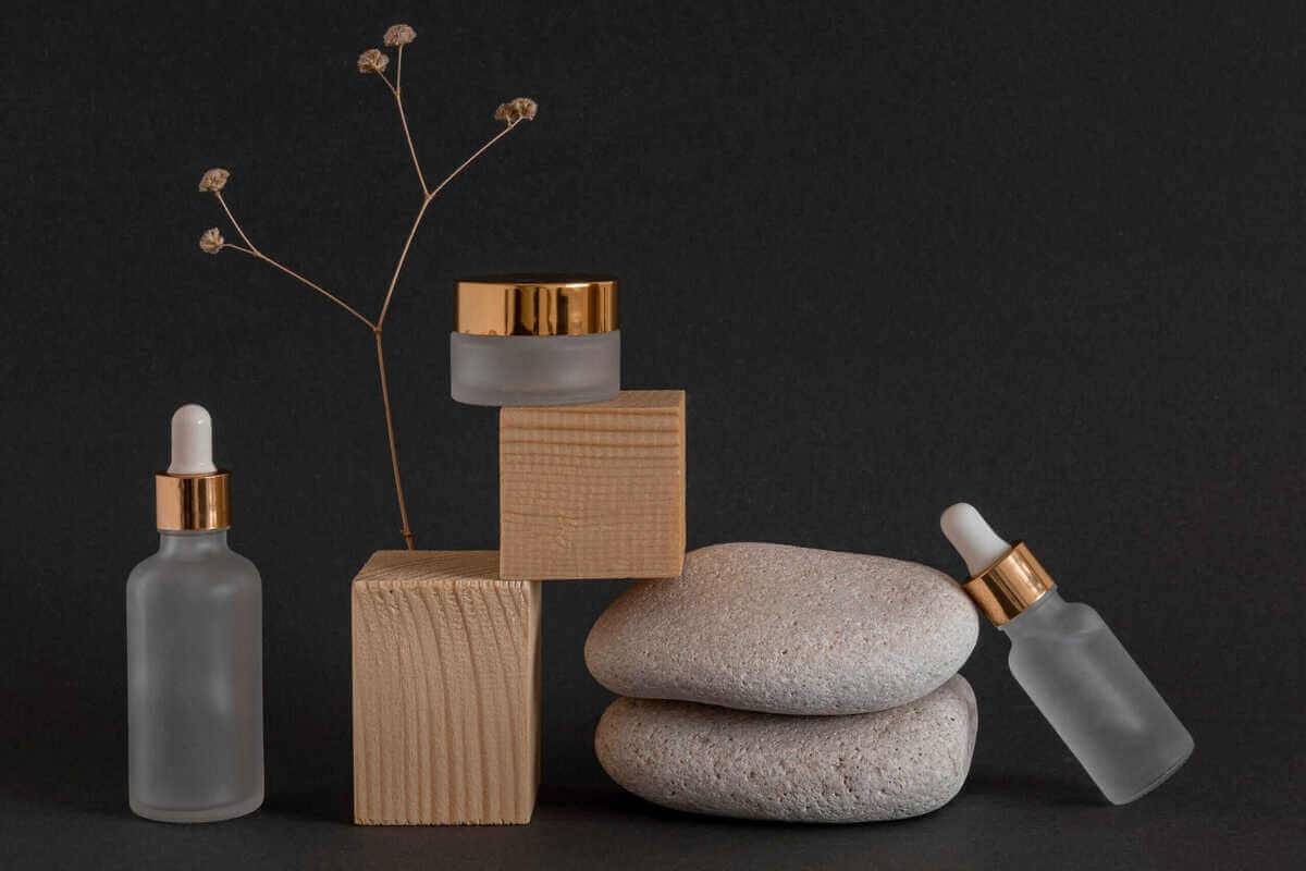 Luxury frosted glass skincare serum bottles with gold accents on stacked stones against dark background